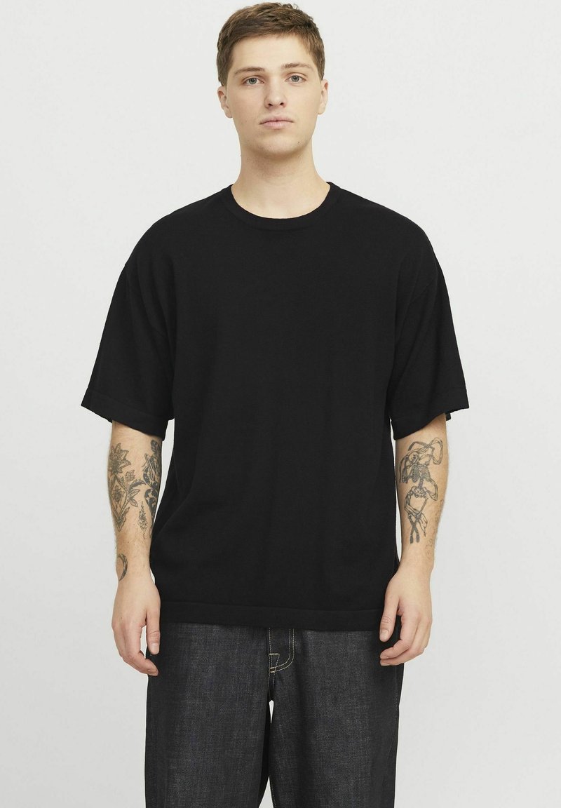 Camiseta de algodón oversized negra con mangas cortas, cuello redondo y corte relajado, combinada con jeans de mezclilla oscura. Sin patrones ni acentos destacados.