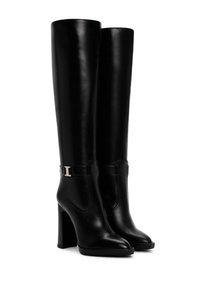 Černé kožené vysoké boty nad kolena s vysokým blokovým podpatkem, špičatou špičkou a dekorativním zlatým sponou na pásku kolem kotníku.