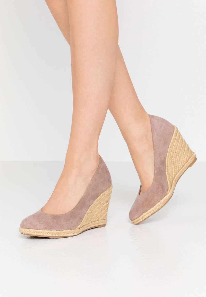 Tacco a wedge in suede marrone con un intersuola in juta intrecciata, dotato di punta tonda e una superficie liscia. Il design è minimalista ed elegante.