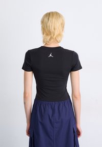 Black fitted short-sleeve t-shirt with a white Jordan logo on the back, paired with a navy blue skirt featuring an elastic waistband.
