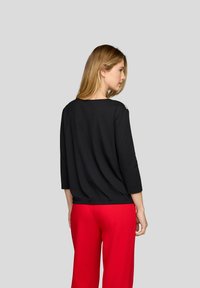 Schwarzes Oberteil mit drei Viertelärmeln und lockerer Passform, rundem Halsausschnitt und gerafftem Taillenteil, kombiniert mit roten weiten Hosen.