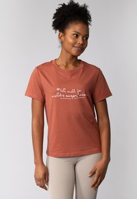 Roodbruine katoenen t-shirt met korte mouwen, heeft een wit gedrukt tekstontwerp. Tekst centraal geplaatst, eenvoudige ronde hals.