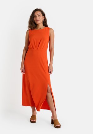 Vestido largo sin mangas de color naranja con una abertura frontal, tejido fluido y cintura ajustada. Combinado con zapatos de tacón bloque marrones y punta abierta.