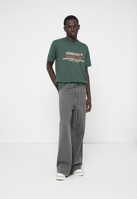 Green t-shirt with a graphic print, paired with gray wide-leg pants. The t-shirt features short sleeves; the pants have a drawstring and a relaxed fit.