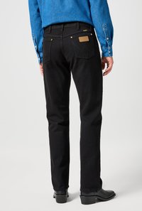 Svarta jeans i denim med rak passform, bakfickor och en brun läderlapp vid midjan. Avslutade med diskreta sömnadsdetaljer.