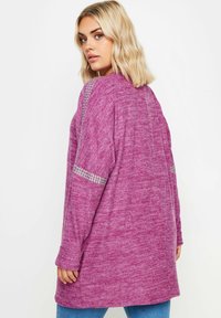 Långärmad topp i strukturerad lila tyg, med silverdetaljer på ärmarna. Avslappnad passform med rundad nederkant.