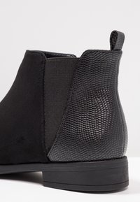 Bota negra hasta el tobillo con parte superior de ante mate, panel texturizado con patrón de reptil, costado elástico y suela de goma plana.