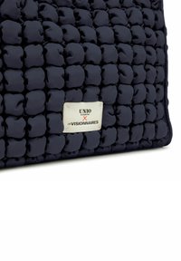 Bolso acolchado de color azul marino con superficie redondeada y texturizada. Presenta una placa de logo plateada con la marca "UNIO" y "LES VISIONNAIRES".