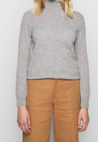 Gray turtleneck sweater made of knit material, featuring long sleeves and a relaxed fit, paired with light brown high-waisted trousers.