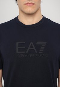 Ναυτικό μπλε βαμβακερή μπλούζα με ματ μαύρο λογότυπο EA7 Emporio Armani στο στήθος. Στρογγυλή λαιμόκοψη και κοντά μανίκια. Μαλακή υφή.