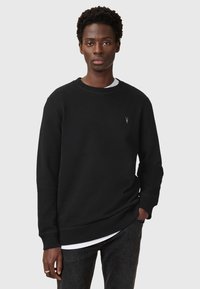 Black sweatshirt made of fleece with a round neckline, long sleeves, and a small logo on the chest. Paired with a white T-shirt beneath.