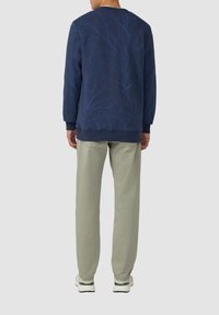 Felpa blu navy con motivo di rami, colletto girocollo e polsini a costine, abbinata a pantaloni verde chiaro e sneakers bianche.