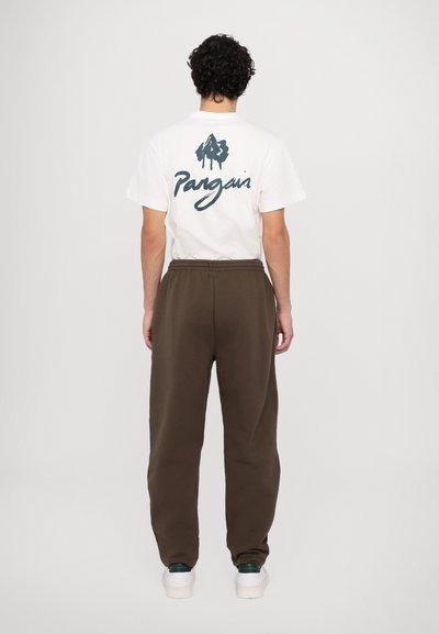 Λευκό βαμβακερό t-shirt με γαλάζιο κείμενο και λογότυπο, συνδυασμένο με καφέ φόρμες, ελαστική μέση, και λευκά παπούτσια με πράσινες λεπτομέρειες.