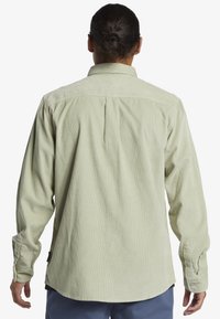 Lichtgroene corduroyshirt met lange mouwen, knoopmanchetten en een rugplooi. Beschikt over een afgeronde zoom en een zijlabeldetail.