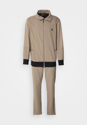 Beige zip-up jacket with a stand collar and black cuffs, paired with matching tapered pants. Made from smooth, lightweight fabric.