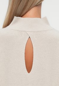 Pulover tricotat bej cu guler înalt și o deschidere în formă de cheie la spate. Material texturat cu o finisare moale.
