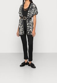 Svart- och vitt mönstrad kimono-liknande jacka med breda ärmar, åtdragen i midjan med ett brett svart bälte, i kombination med svarta åtsittande byxor och skor.