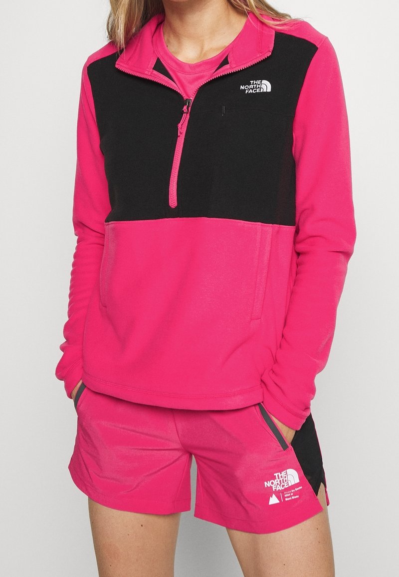 Fleece-pullover i starkrosa med svarta detaljer, design med kvart dragkedja och logotyp. Matchas med rosa shorts med fickor.