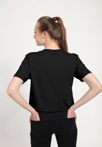 Černé bavlněné tričko s krátkým rukávem, klasickým kulatým výstřihem a volným střihem. Nosit s tmavými džíny, z pohledu zezadu.