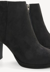 Bottines en daim noir avec fermeture éclair latérale et talons carrés moyens, présentées en gros plan sur un fond blanc.