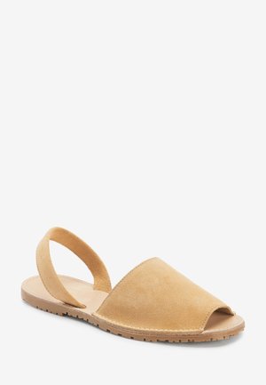 Tan suede slingback sandals with open toe, flat sole, and a wide strap design. Light stitching accents around the edges.