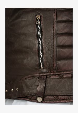 Brown leather jacket featuring a silver zipper pocket, quilted texture, and a snap button detail at the waist with metallic accents.