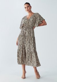 Dzīvnieku raksta gara kleita ar īsām, platām piedurknēm, V veida izgriezumu, pievilktu vidukli un pakāpienveida svārkiem, bēšā krāsā ar melnām svītrām.