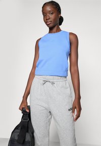 Blå ärmlös topp av bomull, matchad med grå sweatpants med elastisk midja och logotypdetalj, och en svart väska i ena handen.