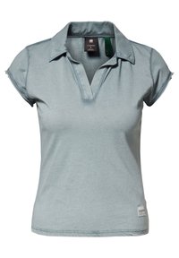 Polo de color azul claro hecho de tejido suave, con cuello, mangas cortas y un ligero escote en V. Presenta una pequeña etiqueta de logo en el dobladillo.
