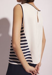 Top bez rękawów z białym przodem i granatowo-białym w pasy tyłem, z dekoltem w kształcie łezki i gładką fakturą materiału.