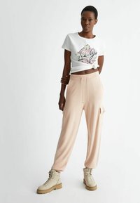 T-shirt bianco in cotone con stampa floreale, abbinato a pantaloni jogger larghi di un rosa pallido con tasche laterali. Stivali beige con lacci.