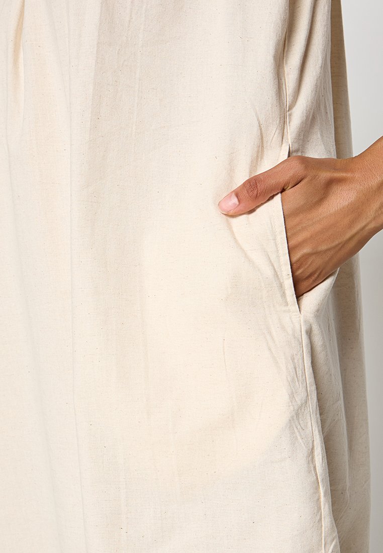 Beige katoenen jurk met een zijzak, zachte textuur en subtiele rimpels voor een relaxte uitstraling.