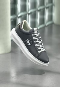 Ανοιχτό γκρι αθλητικό παπούτσι από δέρμα με λευκές λεπτομέρειες, σχέδιο με κορδόνια, διαθέτει λογότυπο και υφασμάτινες λεπτομέρειες στη γλώσσα και τη φτέρνα.