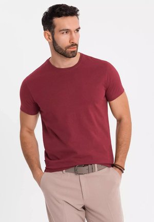 Bordeauxfarbenes T-Shirt mit kurzen Ärmeln aus weichem Stoff, mit Rundhalsausschnitt, schlanker Passform und glatter Textur. Kombiniert mit hellen Hosen.