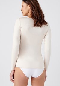 Beige longslub trui met een ronde halslijn en een naadloos ontwerp. Zachte, lichte stof met een gladde textuur. Witte onderkleding zichtbaar.