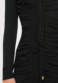 Black long-sleeve dress featuring ruched texture on the bodice and drawstring detail with a gold accent at the end.
