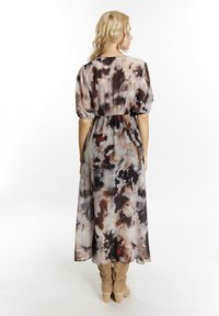 O rochie lungă, vaporoasă, cu un model abstract multicolor, având mâneci bufante, talie elastică și un material ușor.
