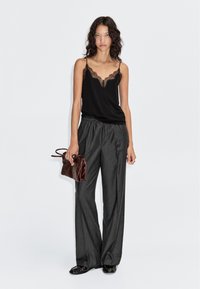 Zwarte cami met kanten rand, gecombineerd met grijs gestreepte wijde broek en een bruine clutch, met een gladde textuur en relaxte pasvorm.