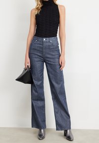 Czarny prążkowany bezrękawnik i ciemnoniebieskie, wysokie spodnie z szerokimi nogawkami, zestawione z błyszczącymi srebrnymi butami na obcasie i małą czarną torebką.