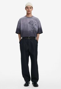 Camiseta de gran tamaño en degradado de gris a negro con un diseño de texto abstracto, combinada con pantalones negros de cintura alta y zapatos negros.