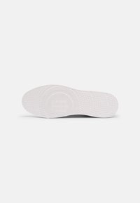 White rubber shoe sole with textured grip, featuring a circular logo pattern in the center. Smooth edges and rounded toe design.