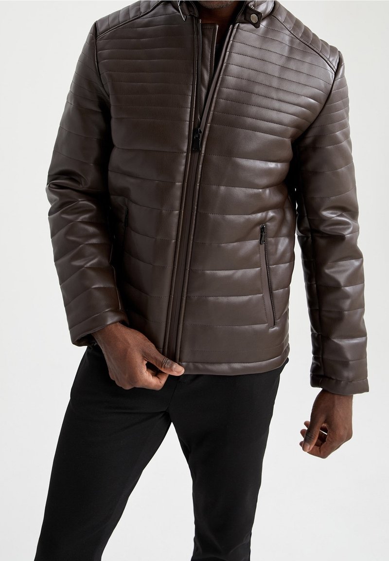 Giacca in pelle trapuntata marrone con zip frontale, colletto alla coreana e tasche laterali con zip. Texture liscia con dettagli di cuciture orizzontali.