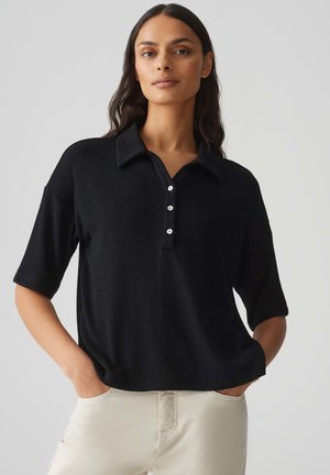 Zwarte polo met korte mouwen en een kraag, met een knoopsluiting en een zachte textuur. Draag het met lichte broek.