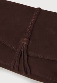 Clutch in suede marrone con dettaglio della tracolla intrecciata e frange. Presenta una texture liscia e una chiusura a pattina con cuciture ordinate.