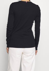 Pitkähihainen musta puuvillapaita pyöreällä kaula-aukkolla, jossa pieni punaisen, valkoisen ja sinisen koriste takaosassa, yhdistetty valkoisiin housuihin.