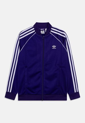 Lilla Adidas træningsjakke med hvide striber på ærmerne, ribbet krave og manchetter, lynlås foran og Adidas-logo på venstre bryst.
