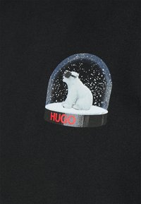 Tejido negro con un oso polar bordado dentro de una bola de nieve. La bola tiene un fondo nevado, con "HUGO" en texto rojo intenso en la base.