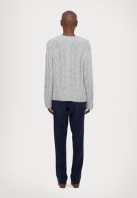 Grey knitted sweater with cable pattern, relaxed fit, round neckline, and ribbed hem. Paired with dark blue trousers.
