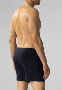 Granatowe bawełniane bokserki o miękkiej teksturze, z elastycznym paskiem w talii i lekkimi bocznymi rozcięciami, prezentowane na nagiej torsie z tyłu.