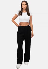 Zwarte, loose-fitting broek met een elastische tailleband, gecombineerd met een aansluitend wit crop top. G gedragen met witte sneakers, gladde textuur.
